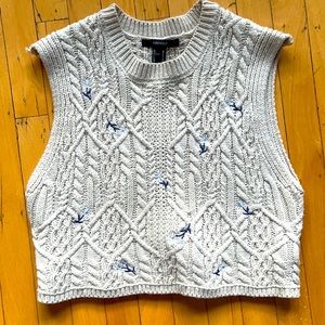 A cream knitted sweater vest embroidered with little flowers.